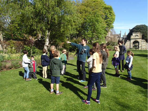 Prof. Will Cresswell with a group of children standing on the grass in St Mary's Quadrangle